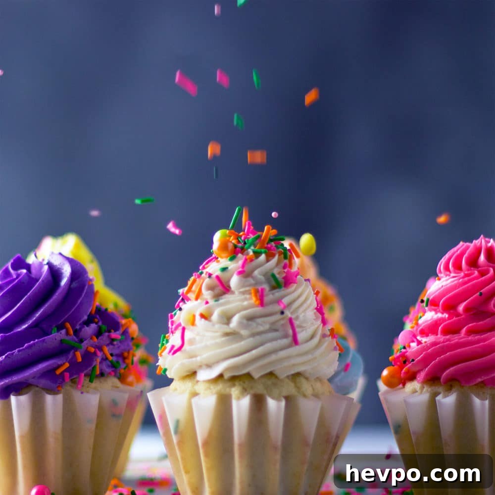 Sprinkles raining down on cupcakes topped with multi-colored buttercream frosting.