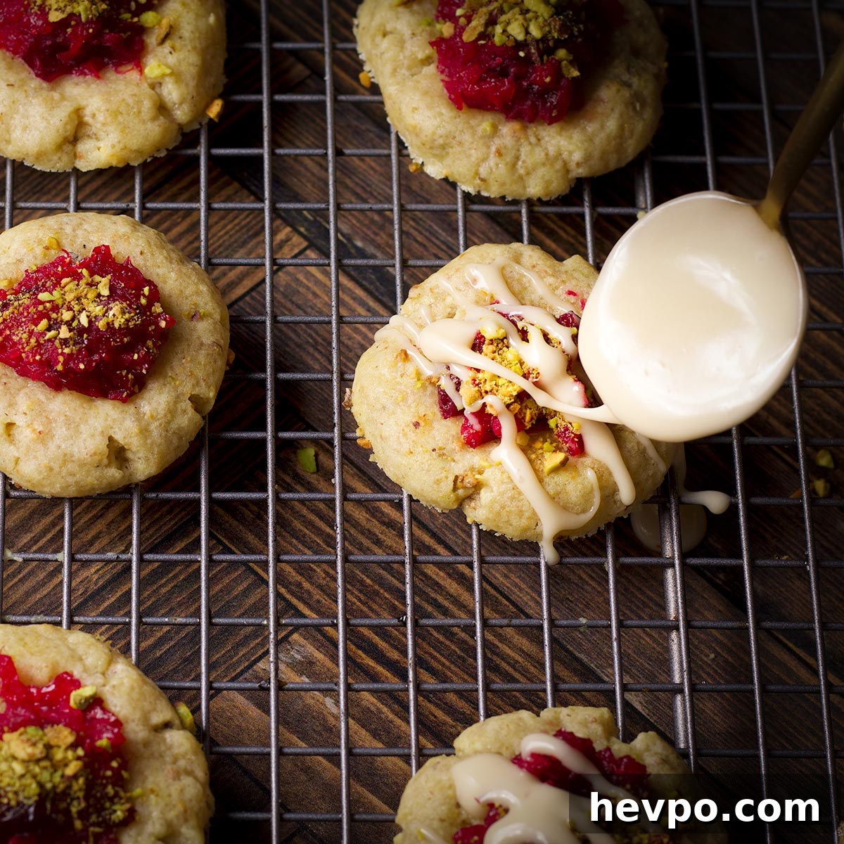 Someone using a small spoon to drizzle vanilla icing over cranberry pistachio cookies.