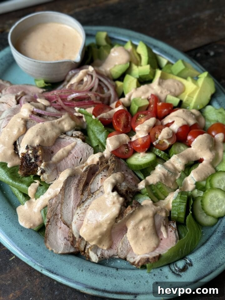 Succulent grilled pork loin salad with fresh vegetables and creamy dressing on turquoise plate.