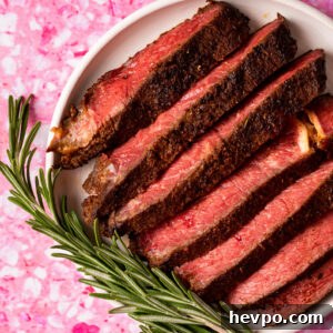 Meal Prep with Sous Vide: Step-by-Step Guide for Perfect Meals 7 Sliced, medium-rare sous vide frozen steak with a dark crust is arranged on a white plate, garnished with fresh rosemary, all set on a bright pink marbled background.