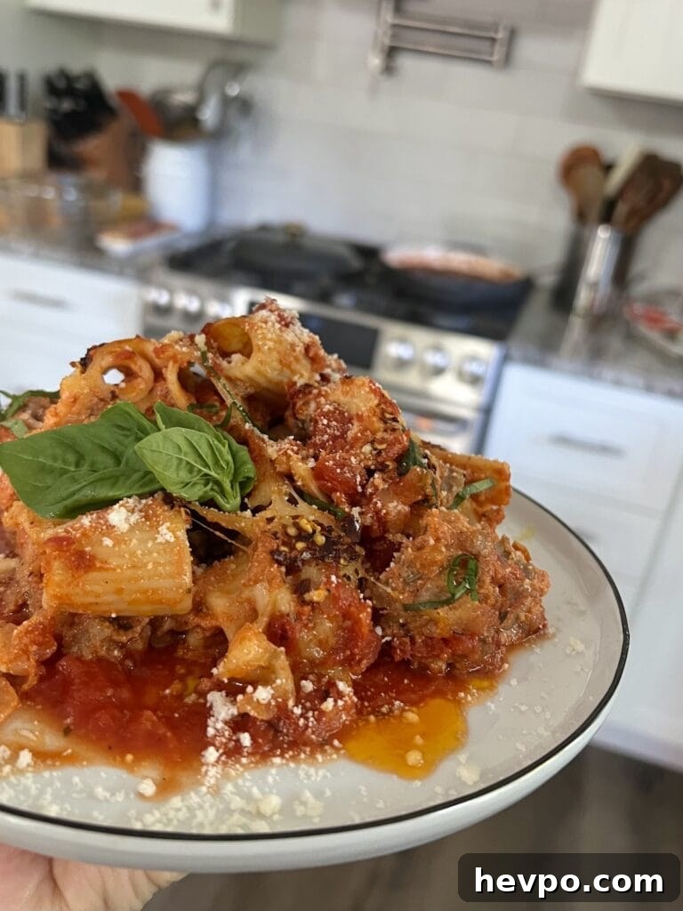 Baked Rigatoni al Forno with Sausage and Beef: Rustic Oven Pasta 2 Close up of rigatoni al forno with basil leaves and kitchen in the background.