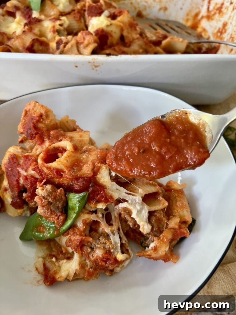 Baked Rigatoni al Forno with Sausage and Beef: Rustic Oven Pasta 18 Adding a spoonful of tomato sauce to a portion of baked rigatoni and sausage in pasta bowl.