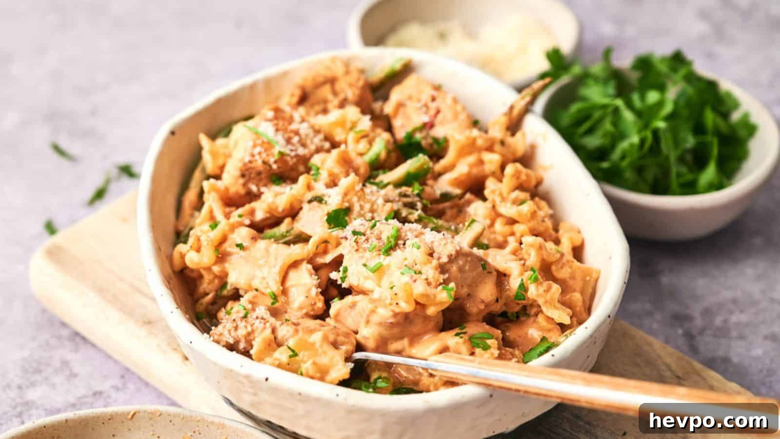 31 Copycat Restaurant Recipes for Delicious Nights In 13 A bowl of creamy chicken pasta garnished with herbs, served with a side of rice and a small bowl of fresh parsley.
