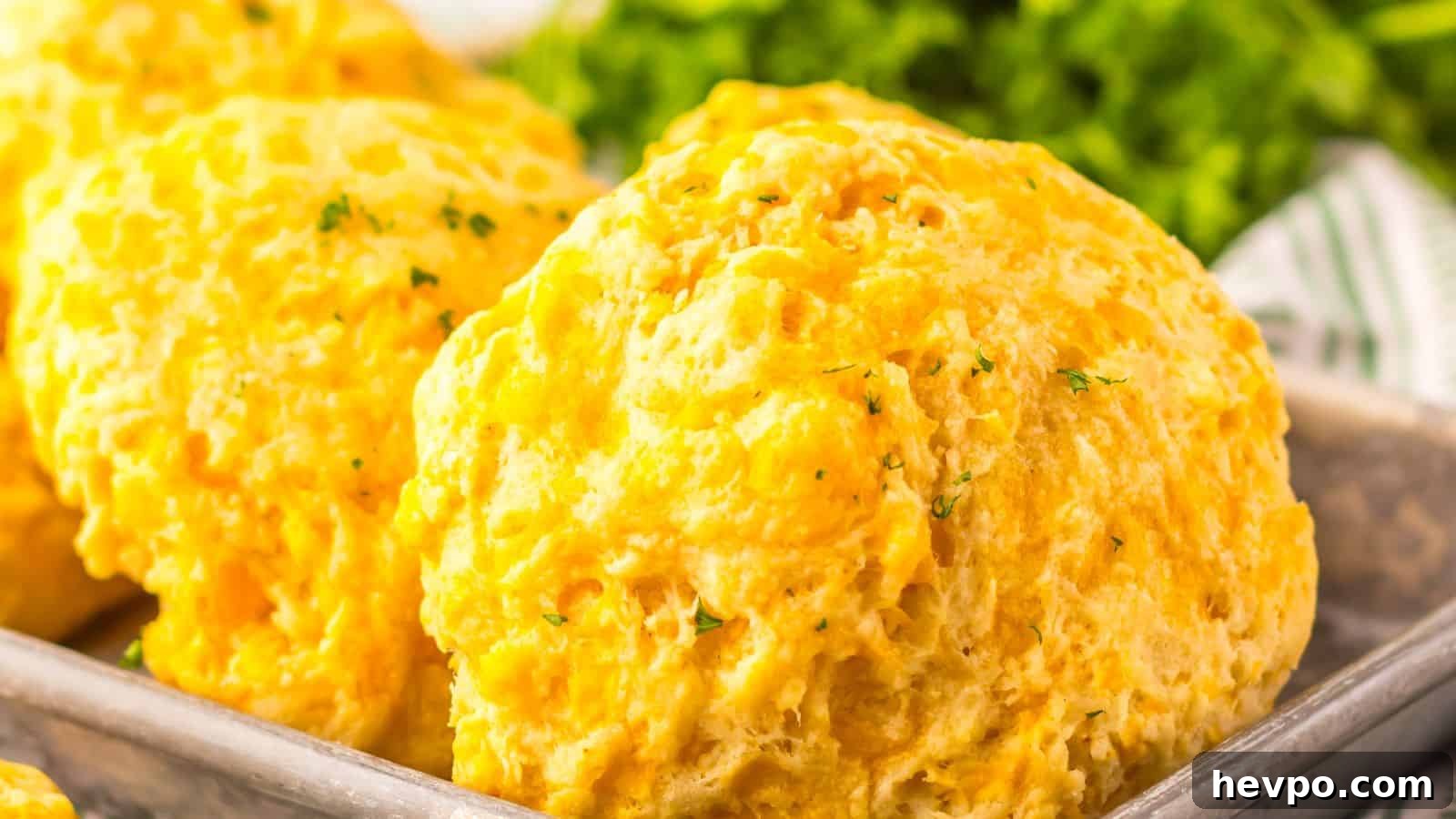 31 Copycat Restaurant Recipes for Delicious Nights In 14 Close-up of fluffy cheddar biscuits topped with herbs on a metal tray, with leafy greens in the background.