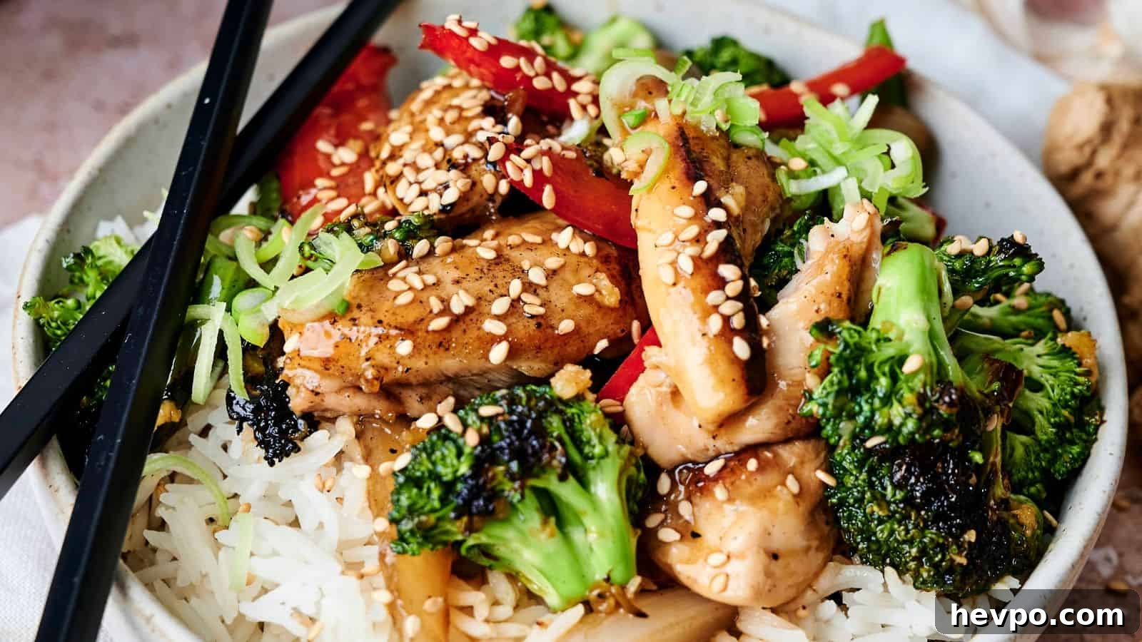 31 Copycat Restaurant Recipes for Delicious Nights In 16 A bowl of rice topped with broccoli, chicken, red peppers, green onions, and sesame seeds, with black chopsticks resting on the side.