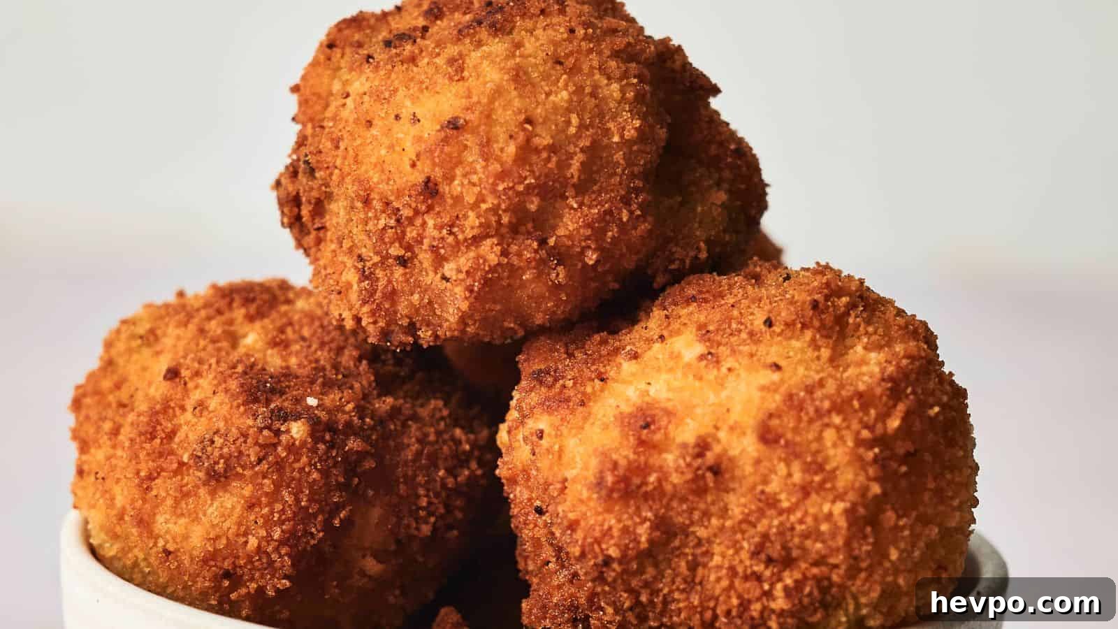31 Copycat Restaurant Recipes for Delicious Nights In 26 A bowl of golden-brown, crispy fried arancini served in a white dish on a plain background.