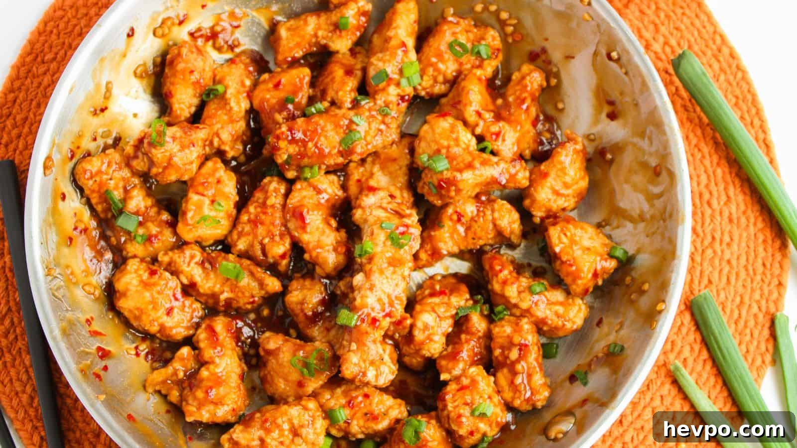 31 Copycat Restaurant Recipes for Delicious Nights In 27 Stir-fried chicken pieces in a spicy sauce, garnished with chopped green onions, served in a round metal dish on an orange placemat.