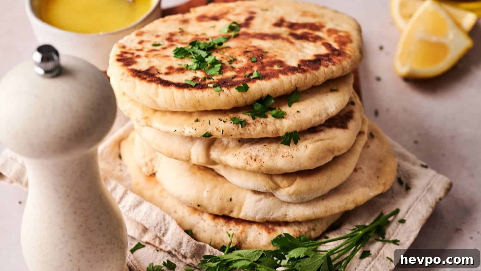 31 Copycat Restaurant Recipes for Delicious Nights In 28 A stack of flatbreads garnished with chopped parsley sits on a cloth, with a white pepper grinder, fresh herbs, a lemon wedge, and a bowl of yellow sauce nearby.