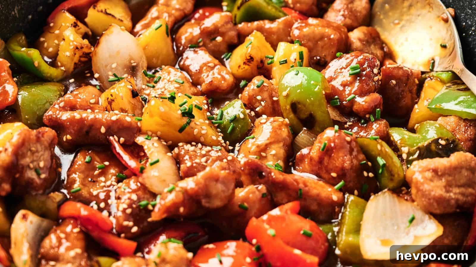 31 Copycat Restaurant Recipes for Delicious Nights In 5 Close-up of sweet and sour pork with chunks of bell peppers, onions, and pineapple, garnished with sesame seeds and chives.