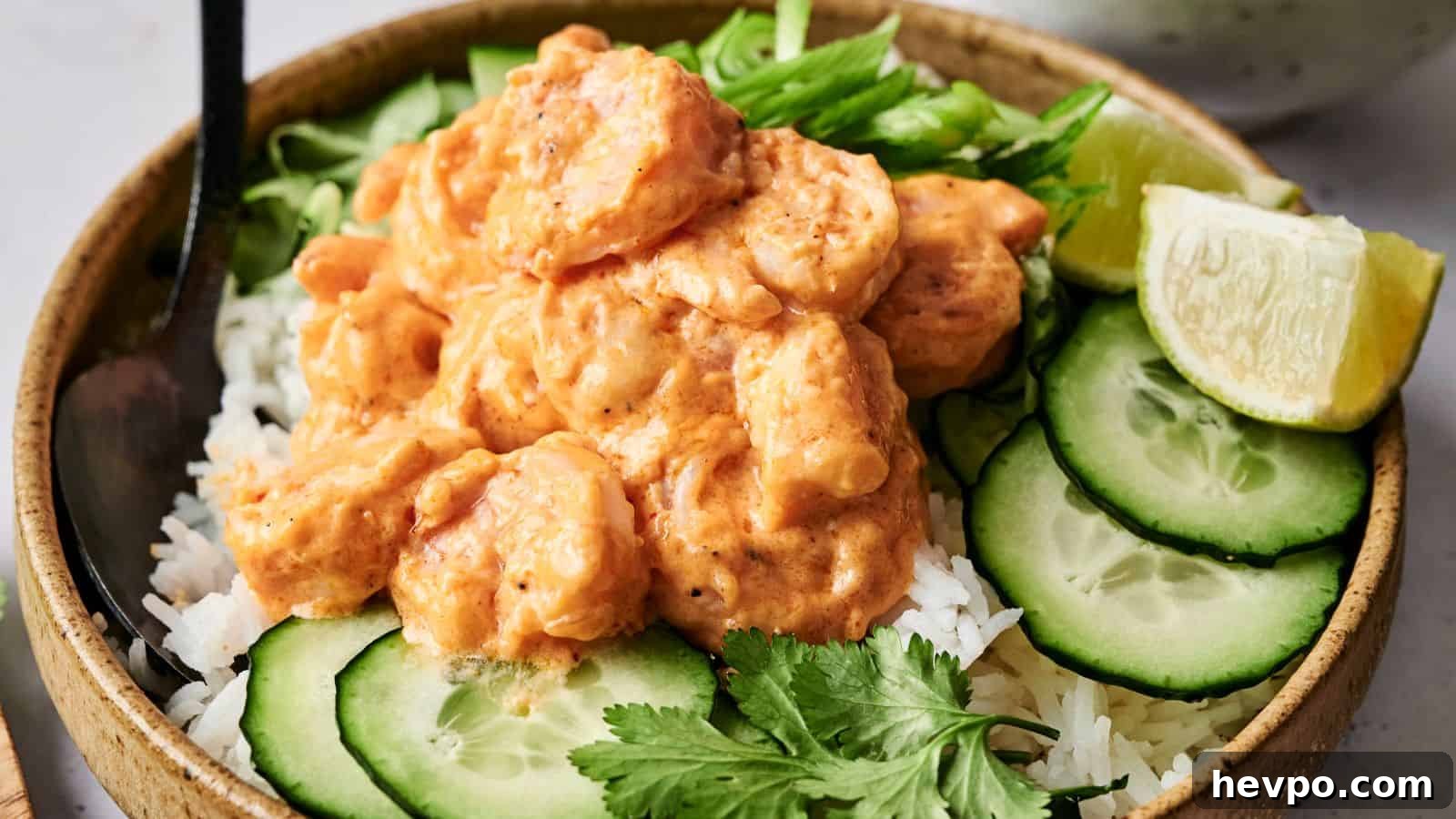 31 Copycat Restaurant Recipes for Delicious Nights In 9 A bowl of rice topped with shrimp in a creamy sauce, garnished with cucumber slices, lime wedge, cilantro, and sliced green onions.