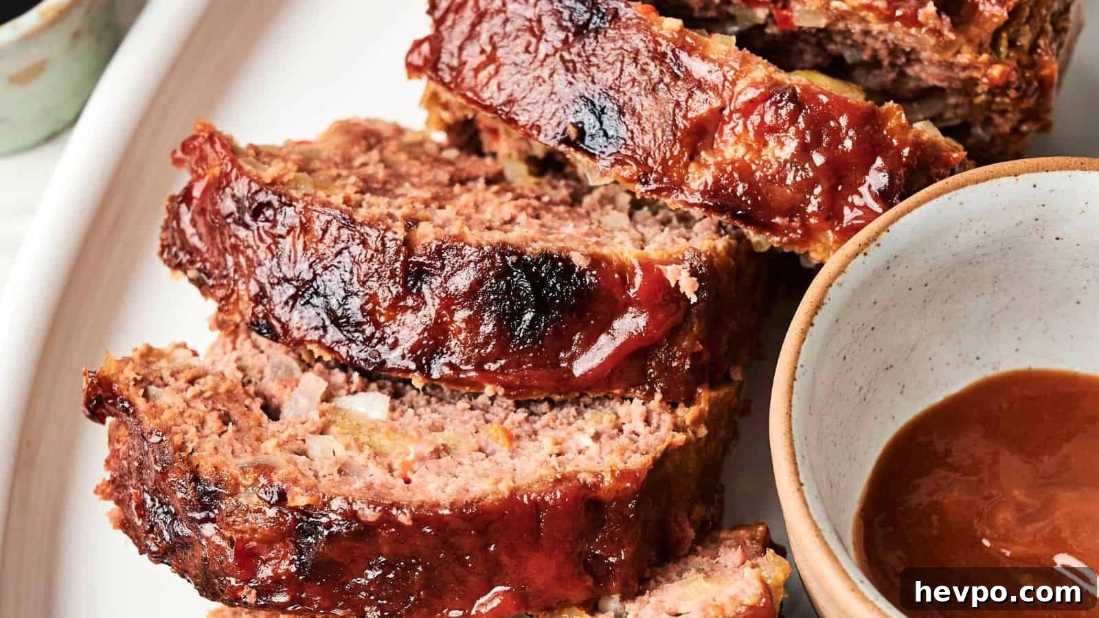 31 Copycat Restaurant Recipes for Delicious Nights In 10 Three slices of glazed meatloaf are arranged on a plate next to a bowl of brown sauce.