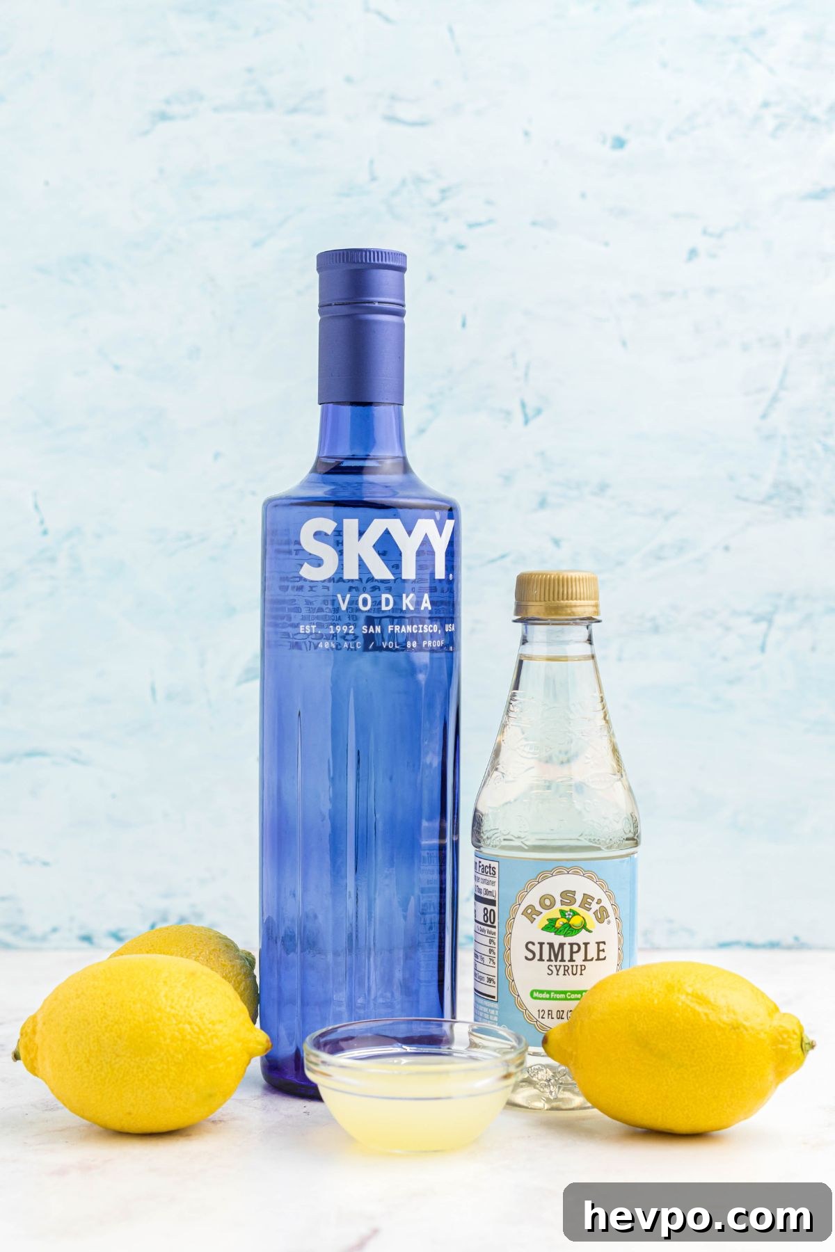 Citrus Lemon Drop Martini Recipe — Zesty Cocktail Guide 3 Bottles of vodka and simple syrup, with a small bowl of lemon juice on a marble table.