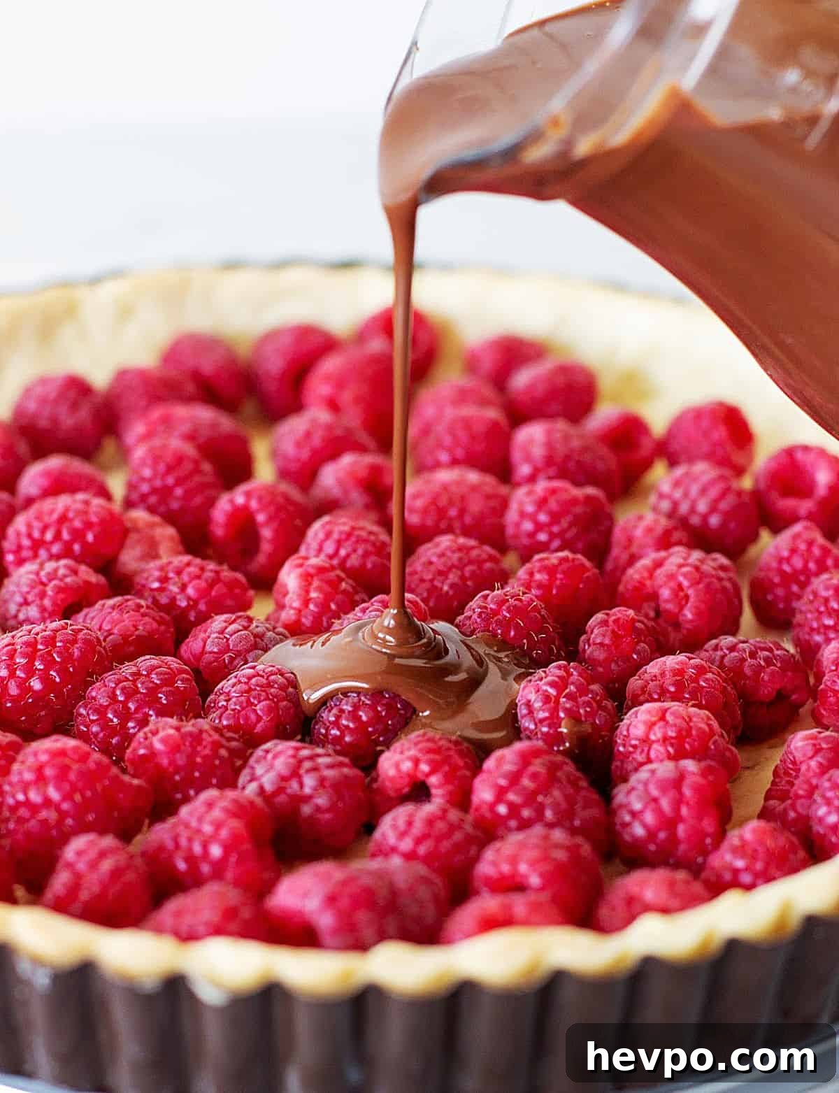 Pouring chocolate filling onto tart crust filled with fresh raspberries.