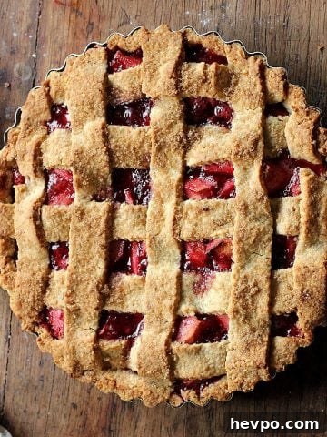 Whole apple raspberry lattice pie on a vintage wooden table.