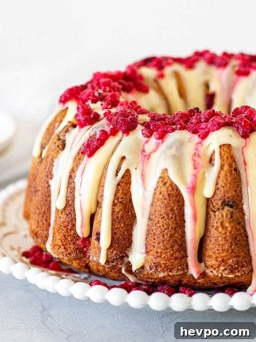 Glazed white chocolate raspberry bundt cake on a white plate, grey background.