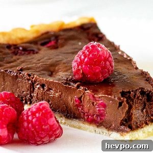 Close up slice of chocolate raspberry tart on a white plate with fresh raspberries.