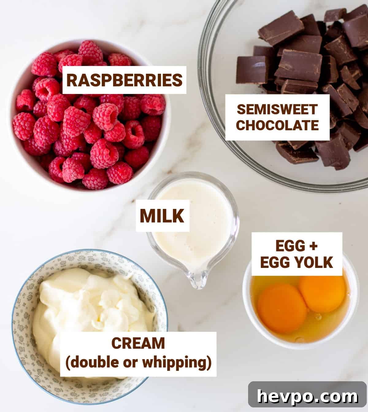 Raspberries, chocolate eggs and cream in bowls on white surface