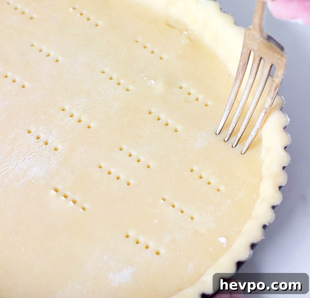 Pricking tart crust with fork, white counter.