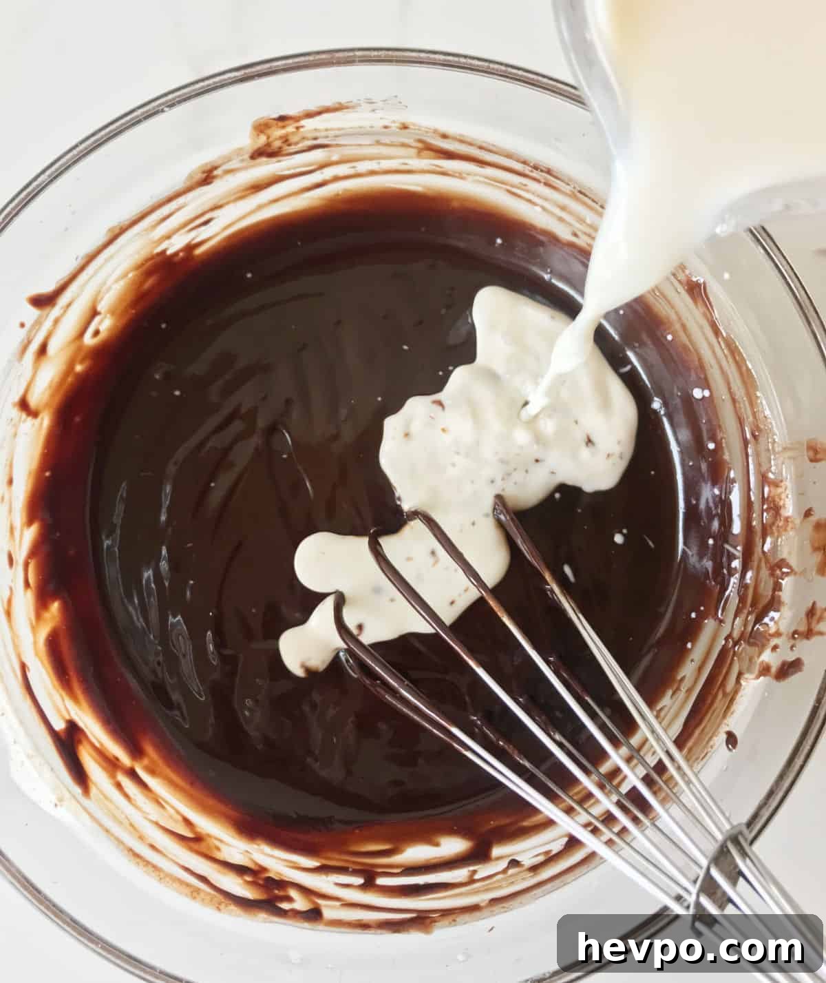 Pouring milk to a glass bowl with a chocolate mixture. White surface. Top view image. 