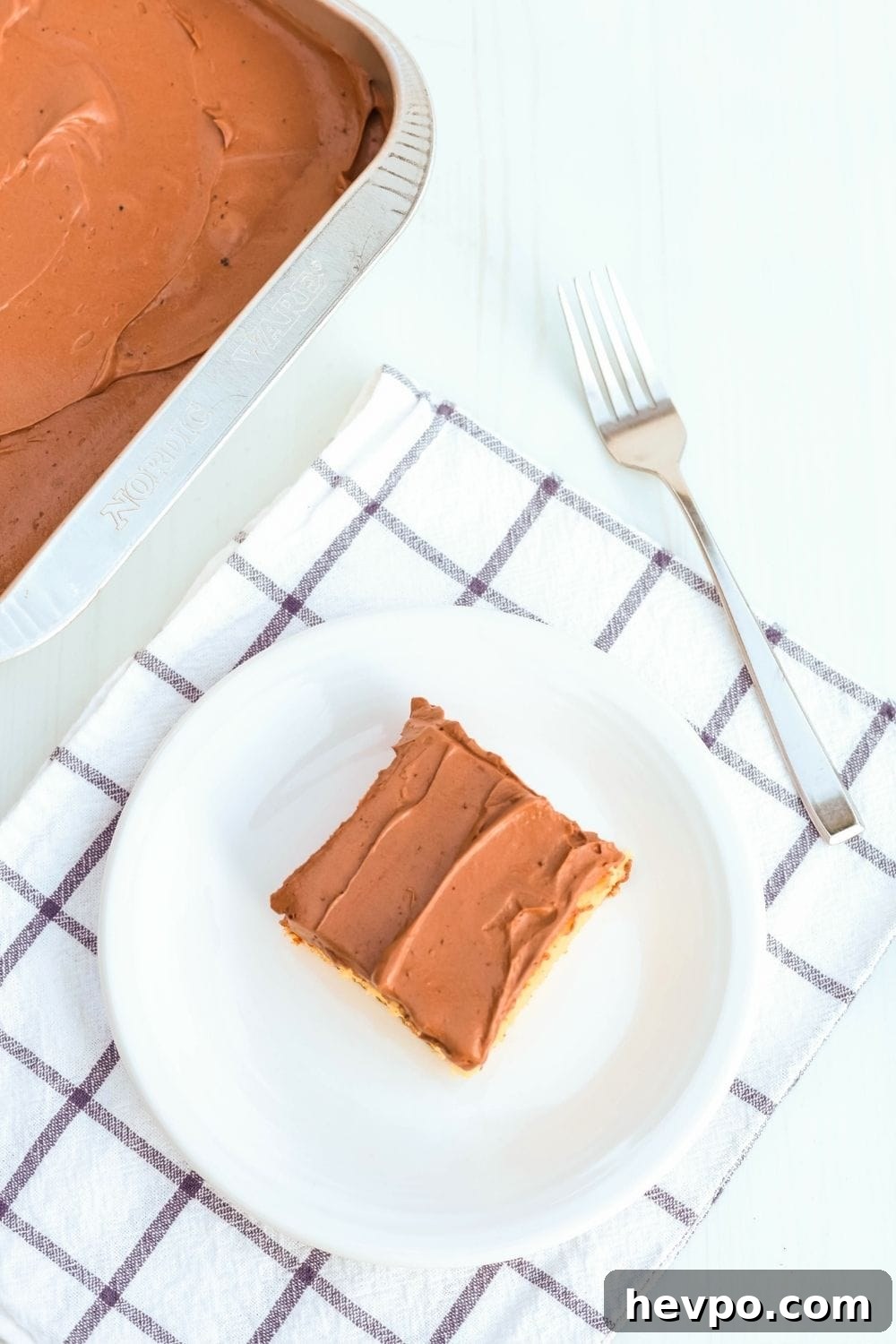 overhead view of a white plate serving a slice of Dream Whip cake. A fork and the pan of remaining cake are in the background.