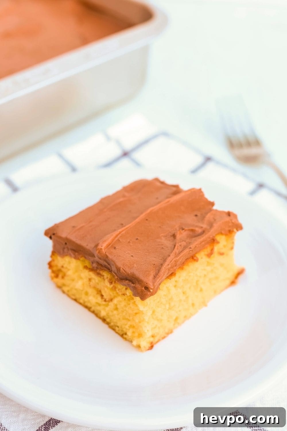 a slice of Dream Whip cake, topped with Dream Whip frosting, served on a white plate. In the background is the pan of remaining cake, as well as a fork.