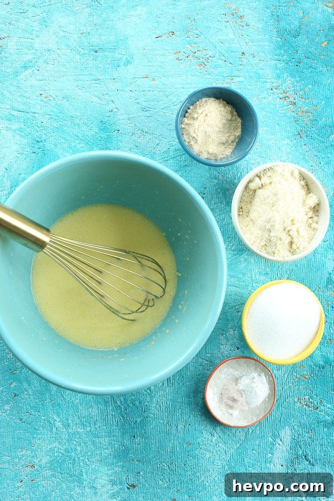 Keto Gluten-Free Sugar-Free Lemon Loaf Cake Recipe 5 an overhead shot of wet ingredients in a turquoise bowl with a whisk, surrounded by dry ingredients in separate bowls