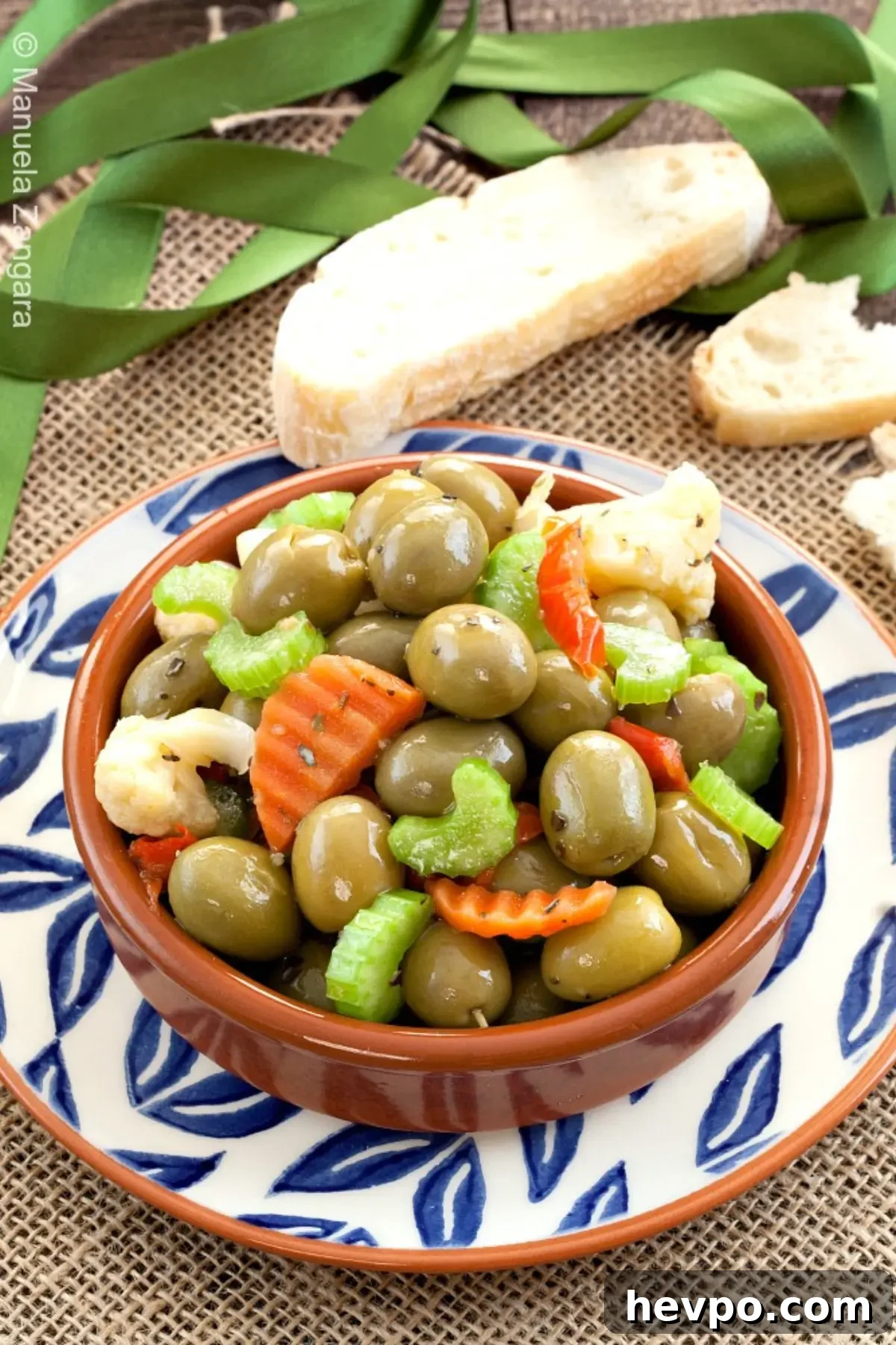 Bowl of Olive Schiacciate with green olives, celery, and pickled vegetables served with sliced bread.