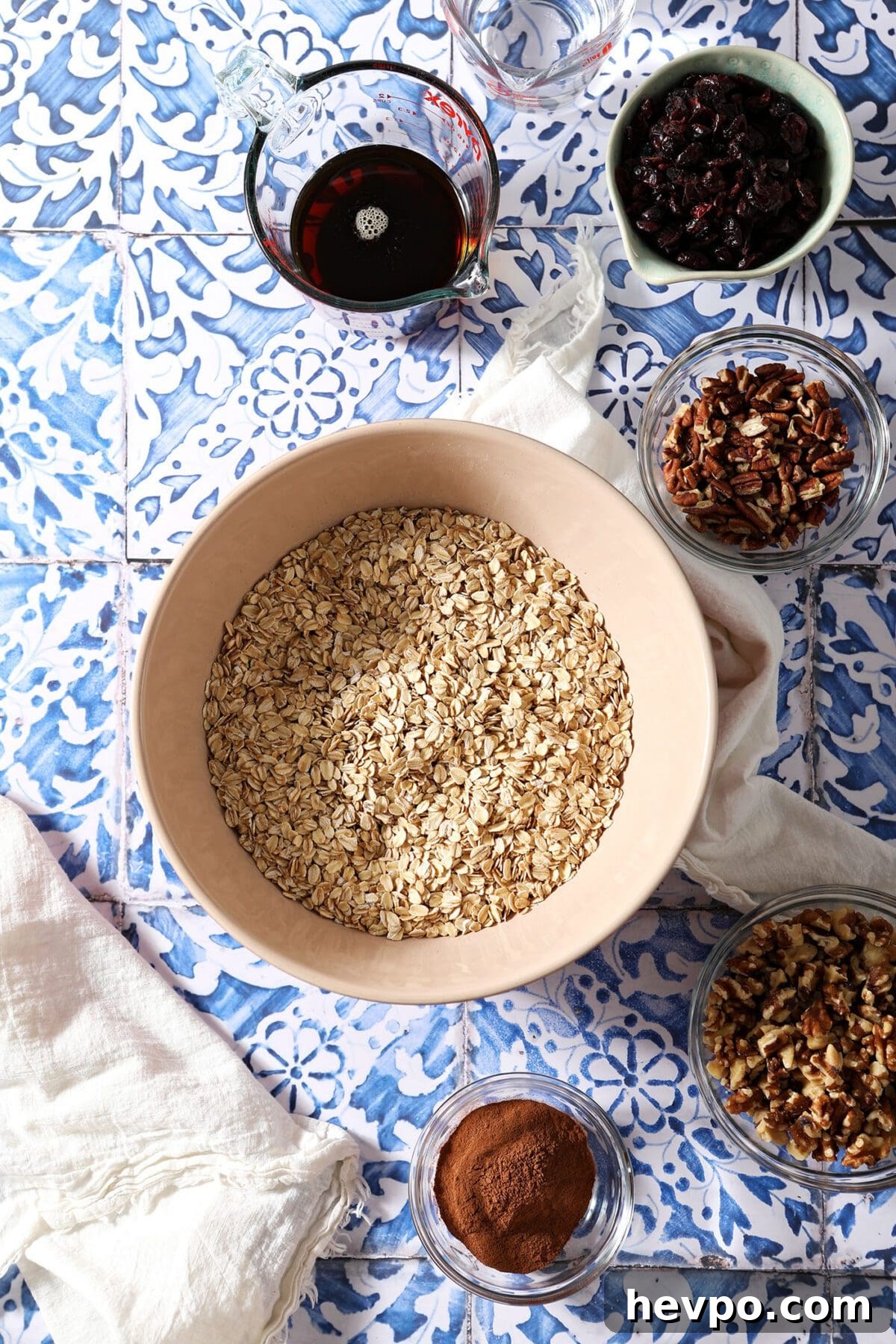 Bowls of ingredients to make maple nut granola on a blue tile surface