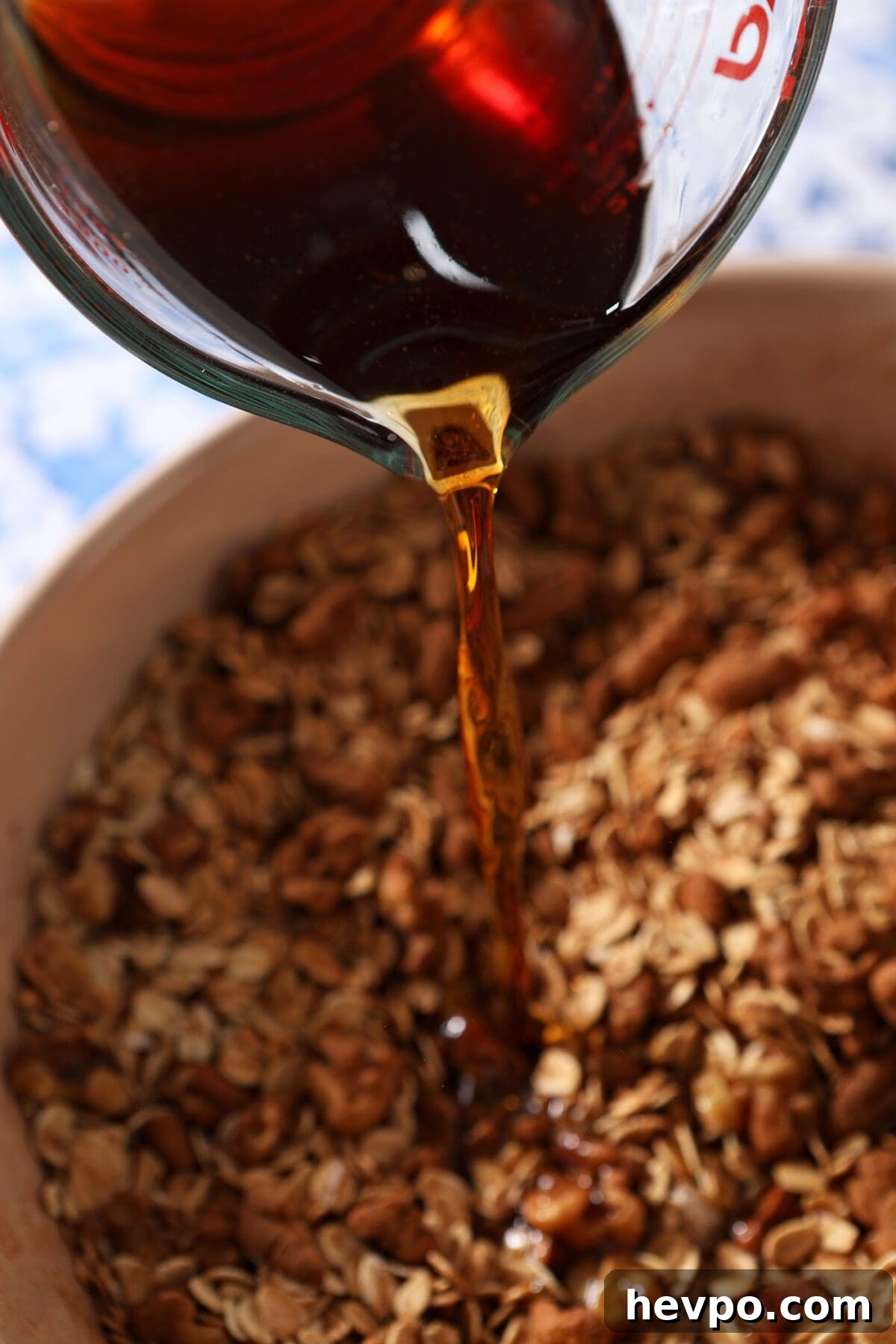A maple-water mixture pours on top of granola ingredients before mixing
