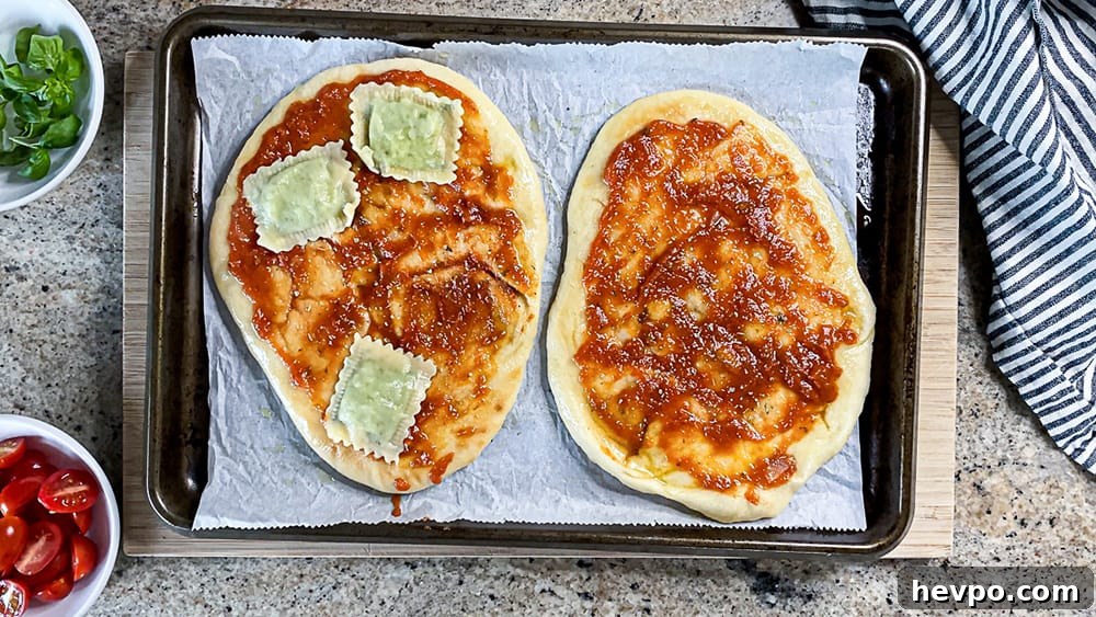 Two pieces of naan covered with pizza sauce and three raviolis on baking sheet.
