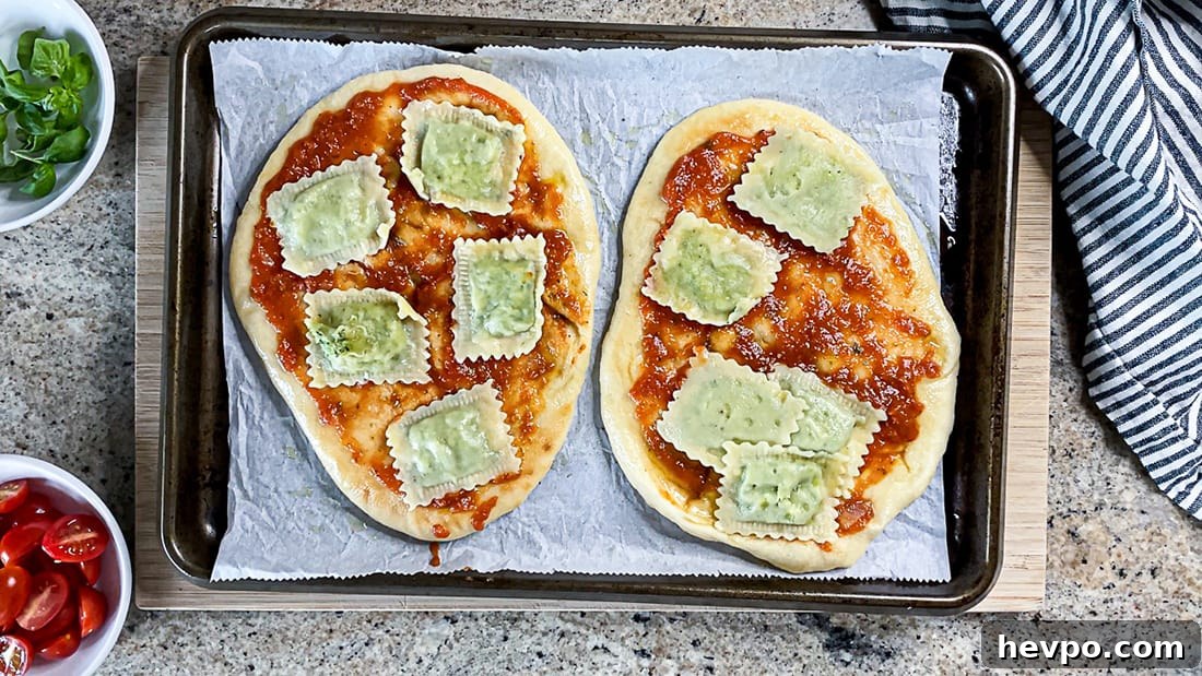 Top shot of naan topped with pizza sauce and raviolis on baking sheet.