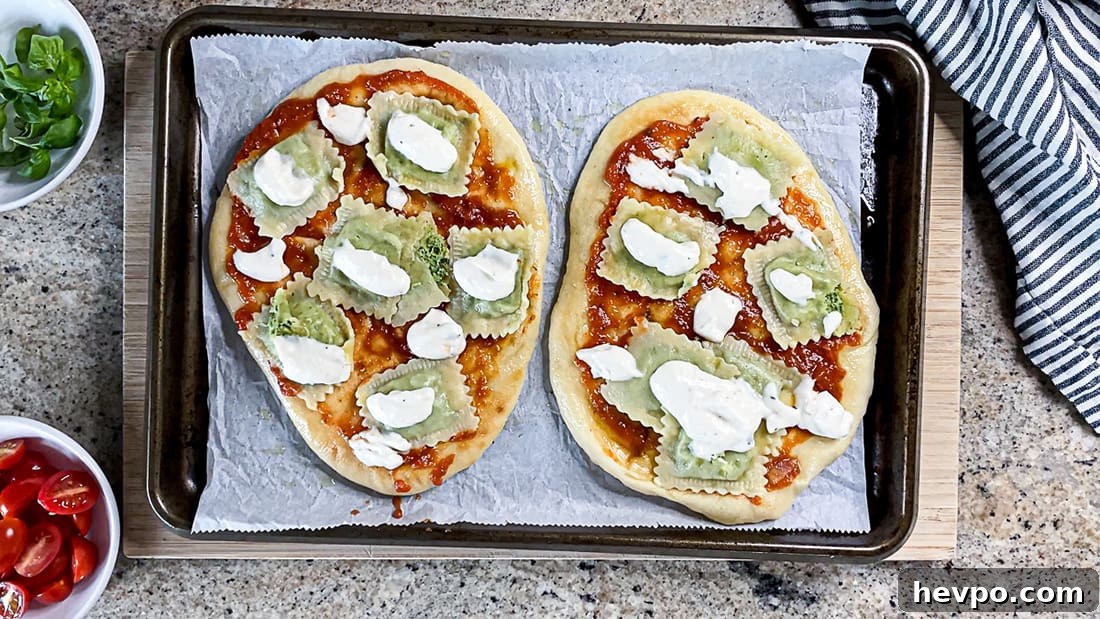 Two flatbread pizzas with ravioli, tomato sauce, and alfredo sauce, on baking sheet.