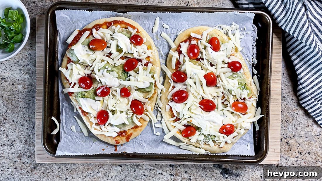 Flatbread pizzas topped with tomatoes and shredded cheese on baking sheet.