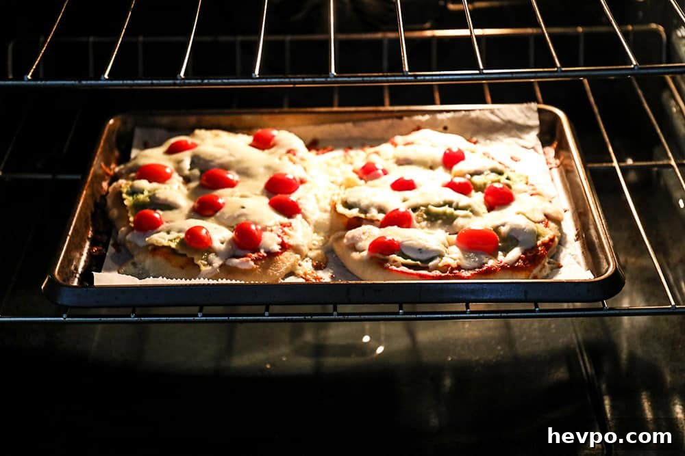 Two ravioli pizzas on flatbread cooking in oven.