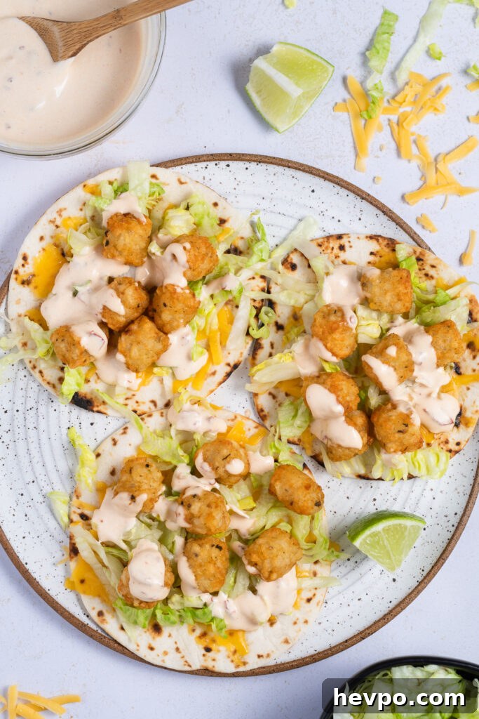 Spicy Potato Soft Tacos Recipe for Flavorful Weeknight Meals 6 White speckled plate with three tacos. The tacos are filled with cheddar cheese, iceberg lettuce, tator tots and creamy chipotle sauce. Wedge of lime on the side
