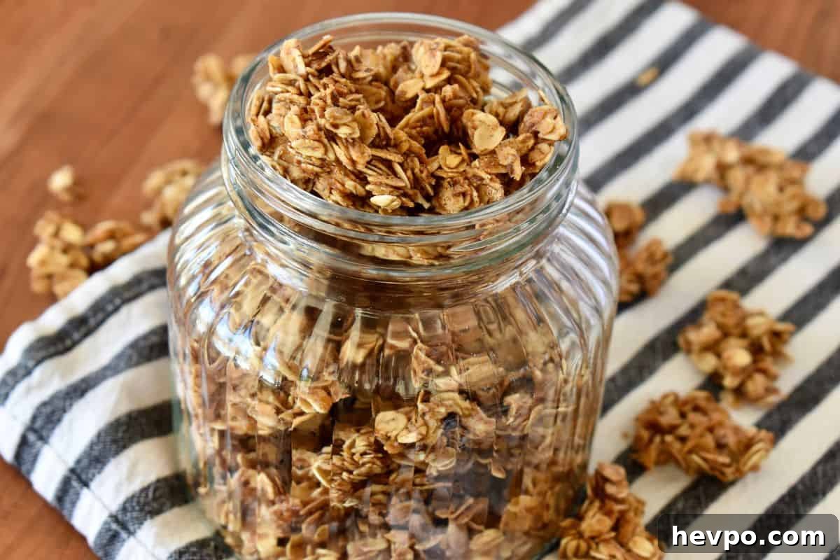 Meal-Prep Breakfast Ideas for Faster, Stress-Free Mornings 3 Granola Recipe without Nuts in a glass container on a countertop on striped napkin.