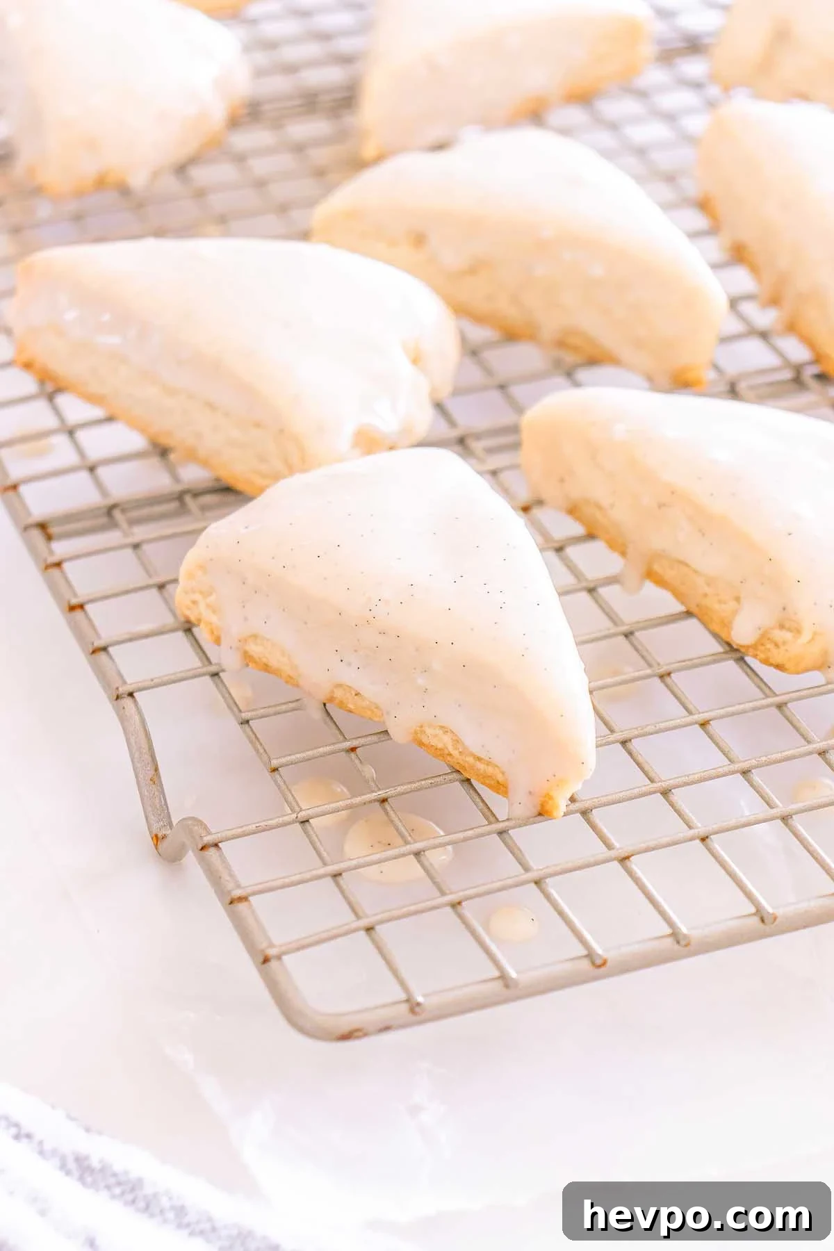 Starbucks Copycat Vanilla Bean Scones, shaped into triangles and topped with white glaze, cool on a rack as icing gently drips onto the surface below.