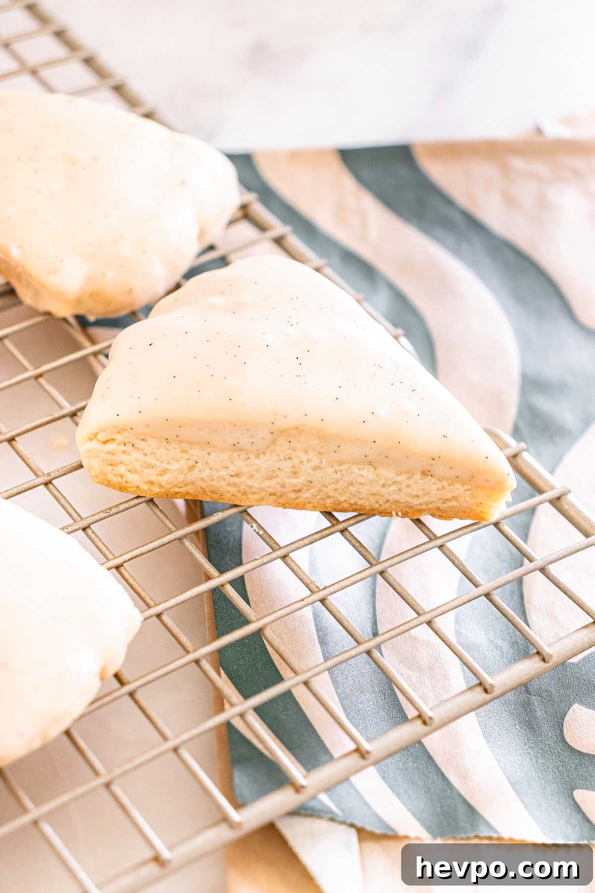 A Starbucks Copycat Vanilla Bean Scone rests on a cooling rack, with a patterned napkin underneath.