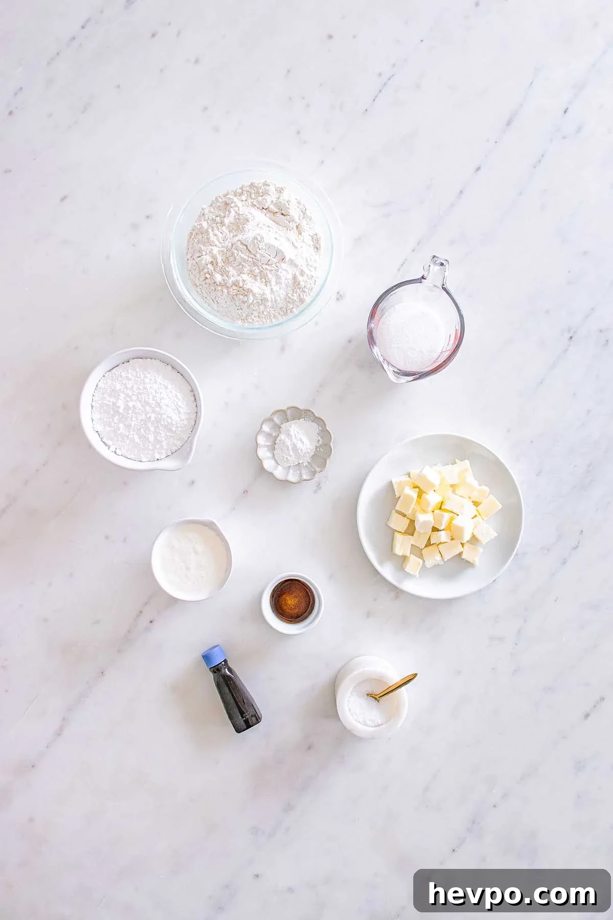 Baking ingredients on a marble surface: flour, sugar, butter cubes, vanilla, salt, and powders in bowls—perfect for making Starbucks Copycat Vanilla Bean Scones.