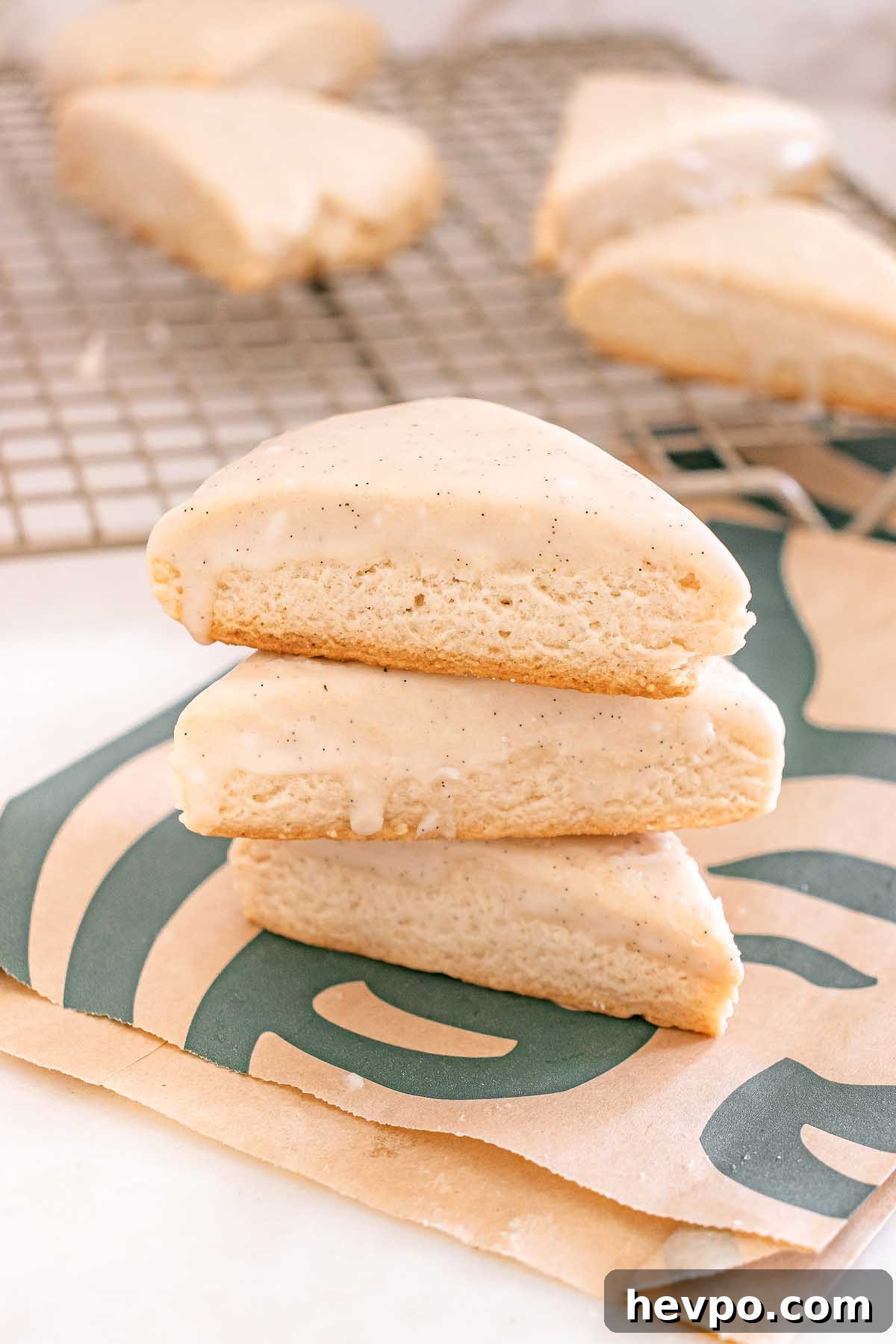 Three Starbucks Copycat Vanilla Bean Scones stacked on a Starbucks bag, with more scones cooling on a rack in the background.