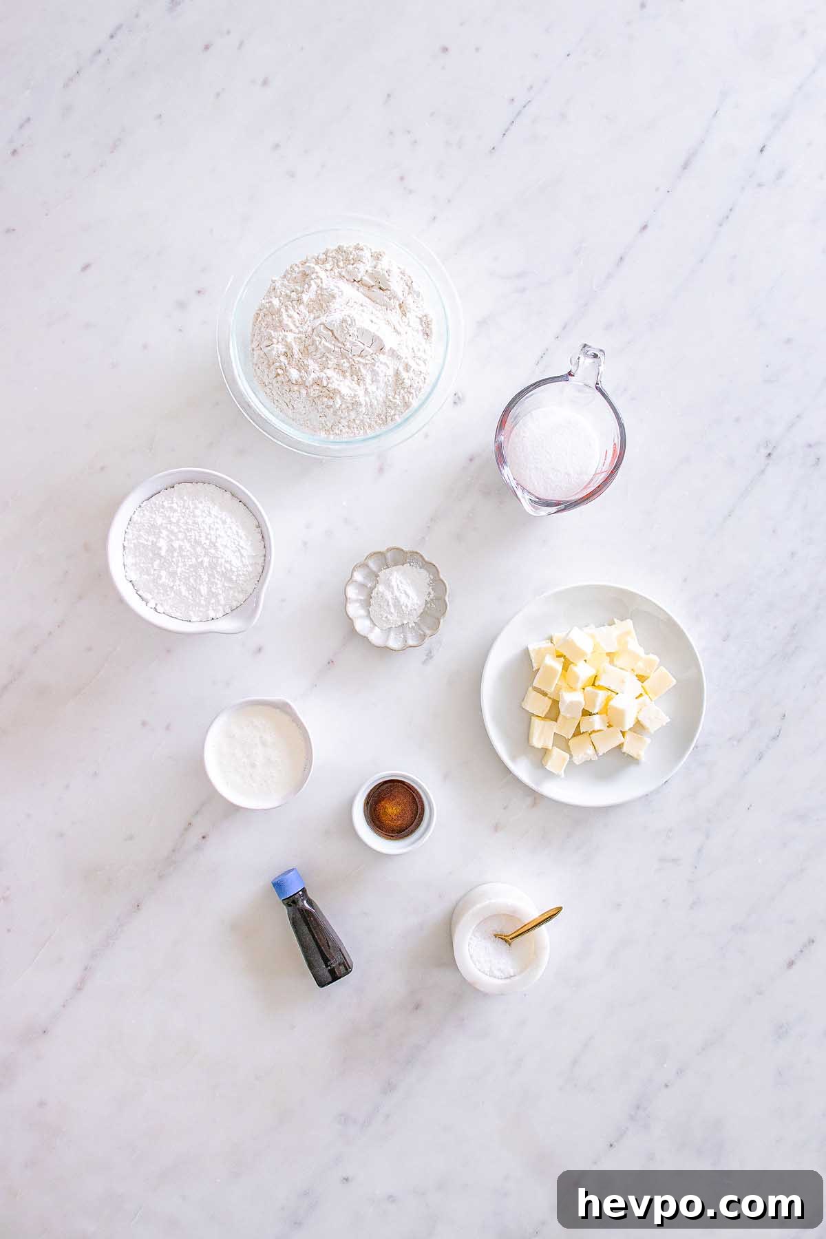 Baking ingredients on a marble surface: flour, sugar, butter cubes, vanilla, salt, and powders in bowls—perfect for making Starbucks Copycat Vanilla Bean Scones.