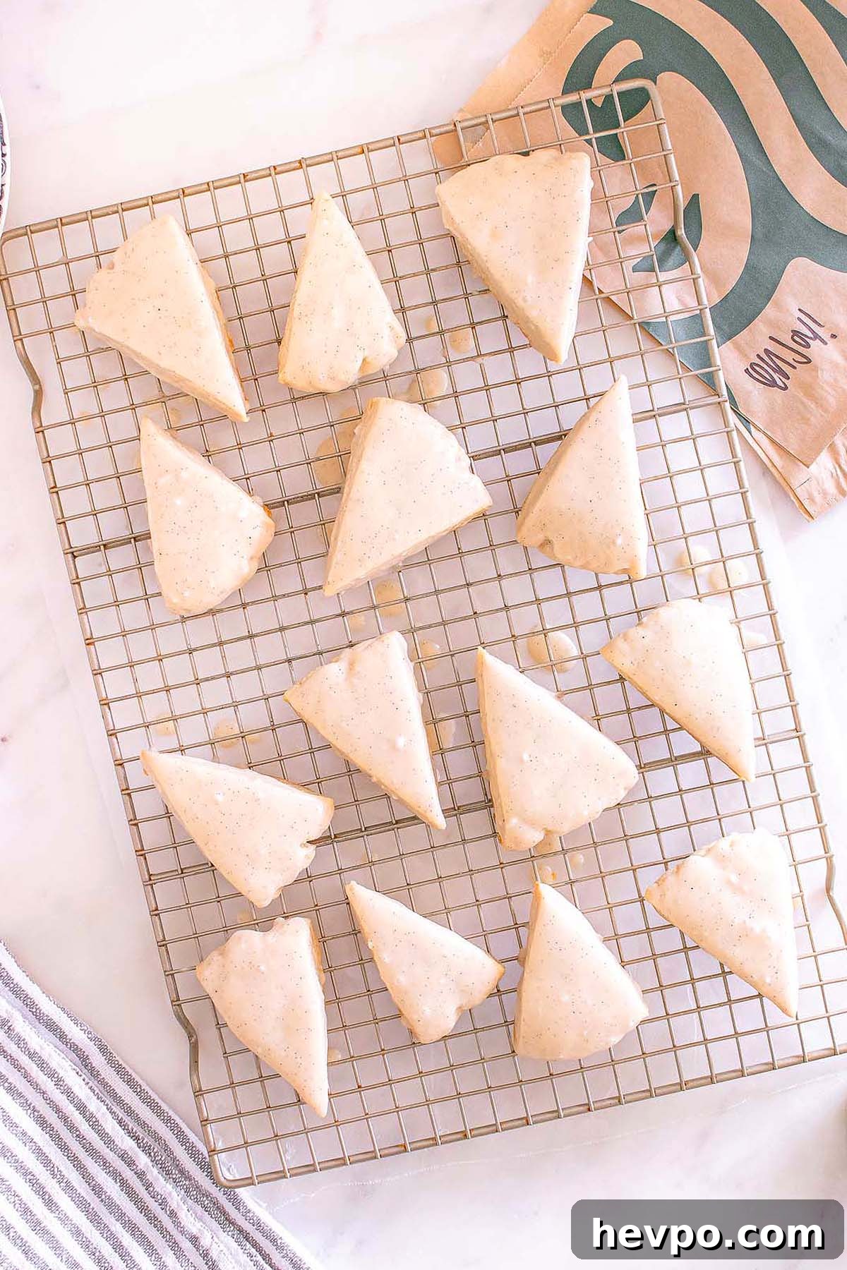Fourteen Starbucks Copycat Vanilla Bean Scones cool on a wire rack, their shiny glaze tempting, with a Starbucks bag visible in the background.