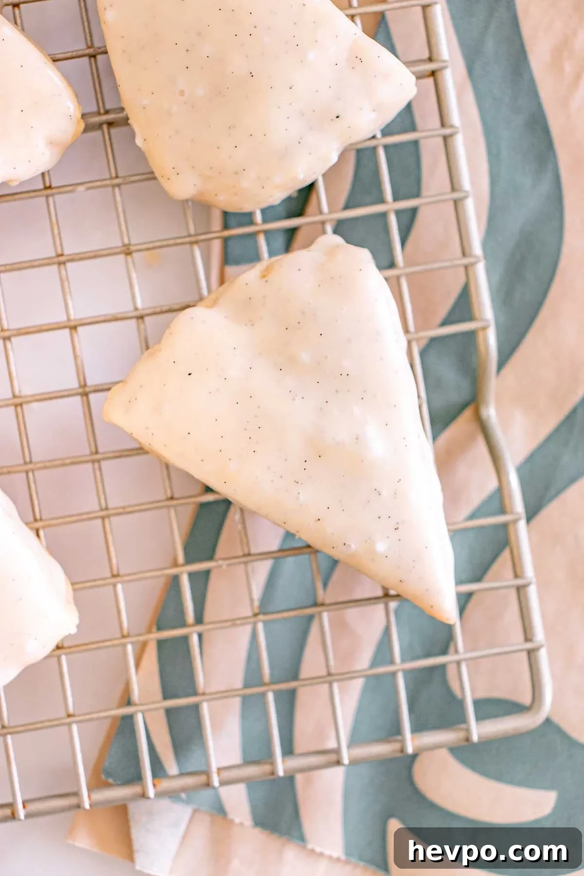 Starbucks Copycat Vanilla Bean Scone, iced and triangular, rests on a cooling rack with a patterned cloth underneath.