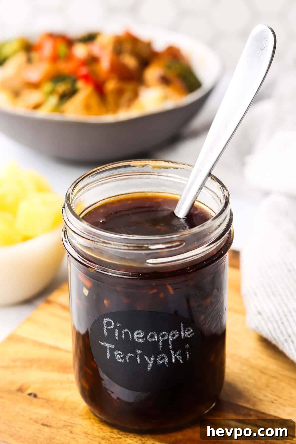 a jar of pineapple teriyaki sauce placed on a cutting board with a spoon in it