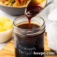 A jar of teriyaki sauce with a spoon drizzling some sauce into the jar to show the consistency.