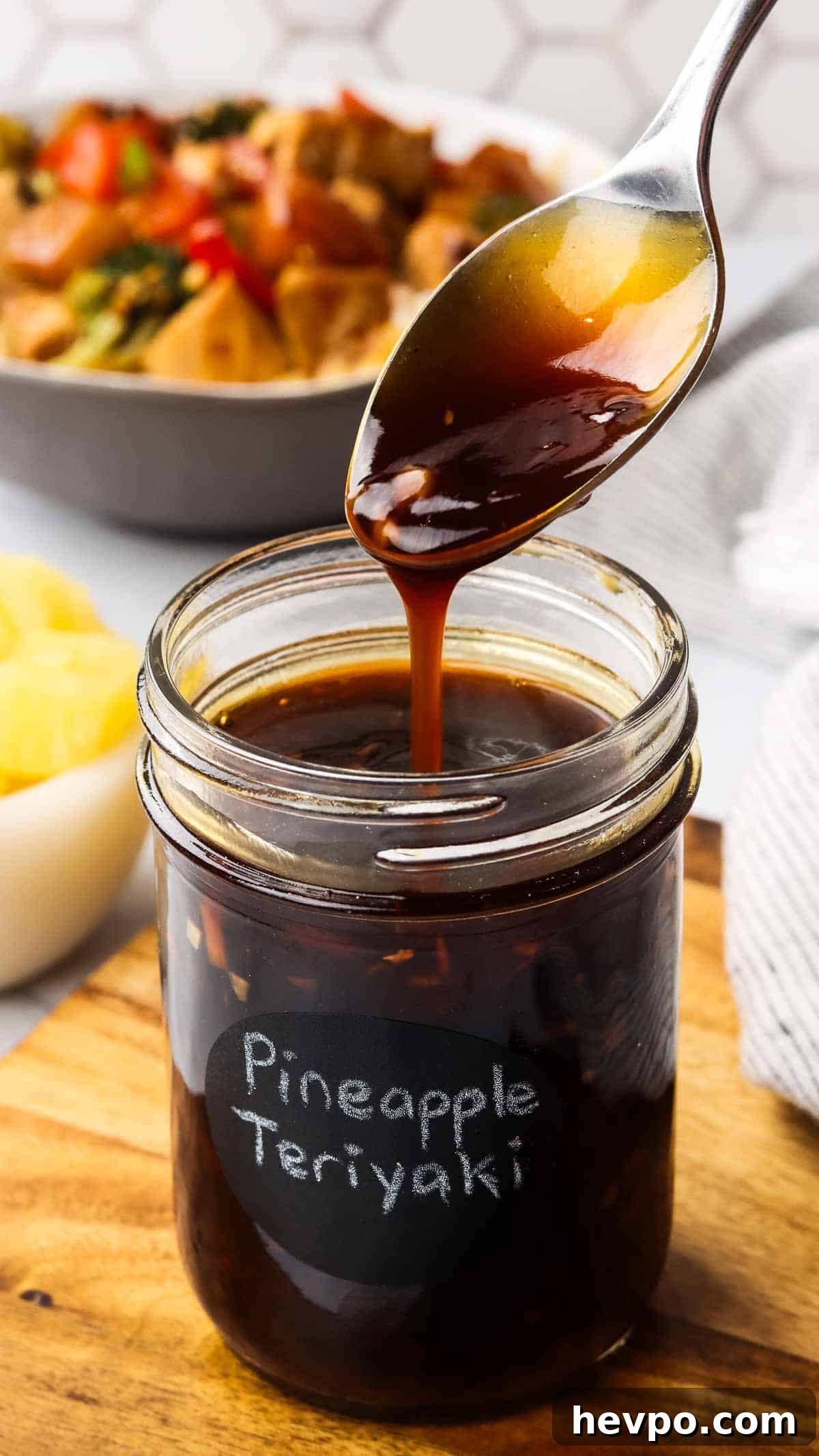 A jar of teriyaki sauce with a spoon drizzling some sauce into the jar to show the consistency.