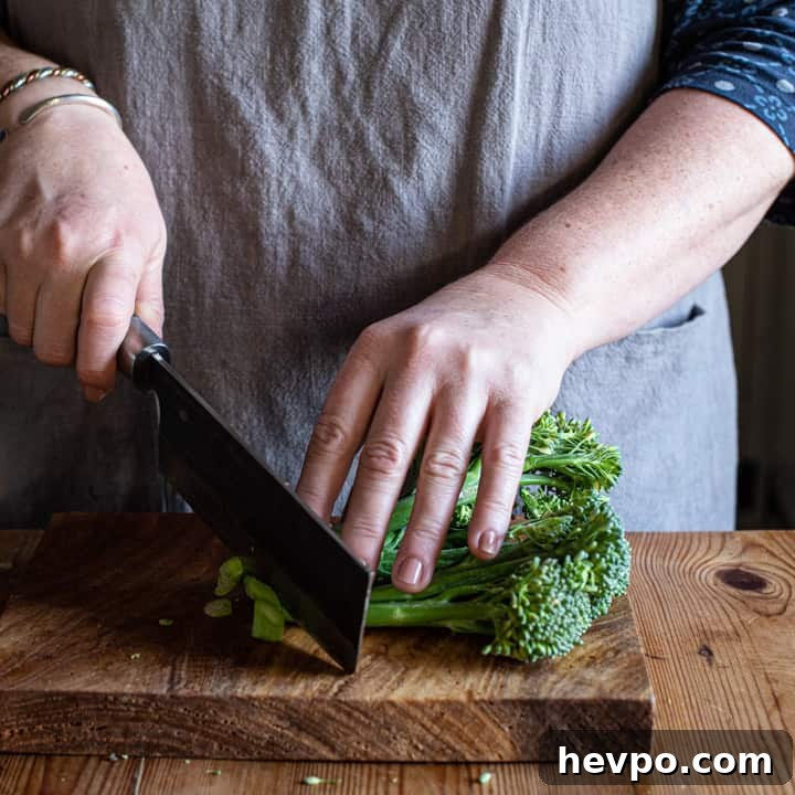 woman's hands chopping broccoli on a wooden board with large Japanese knife
