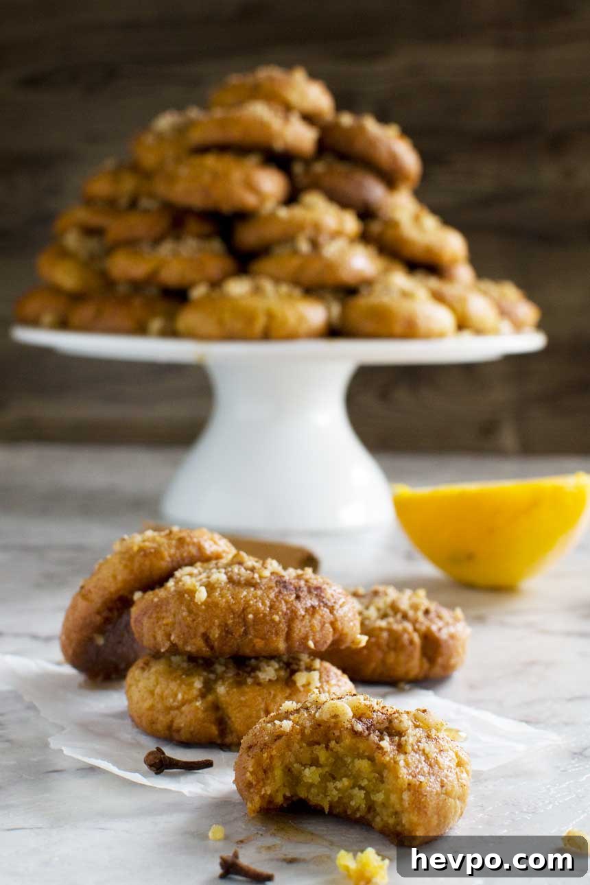 Melomakarona: Traditional Greek Christmas Honey Cookies Recipe 2 A Greek Christmas honey cookie with a bite out of it with more cookies behind it and a pyramid of them on a cake stand behind.