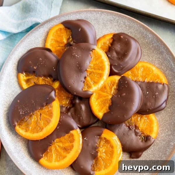 Melomakarona: Traditional Greek Christmas Honey Cookies Recipe 10 A mottled blue plater of candied orange slices dipped in chocolate with oranges and kitchen equipment around them.