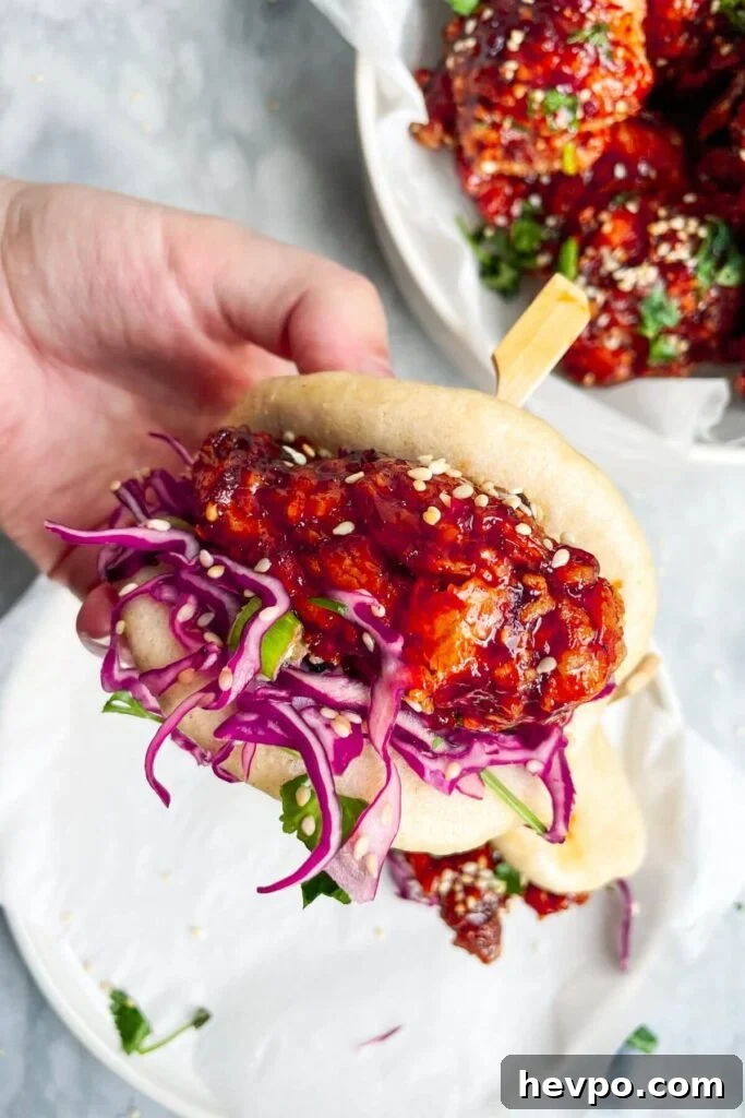 Crispy Korean Fried Chicken Recipe: Extra Crunch & Sticky Sauce 13 Hand holding up a bao bun filled with Korean fried chicken and red cabbage slaw.